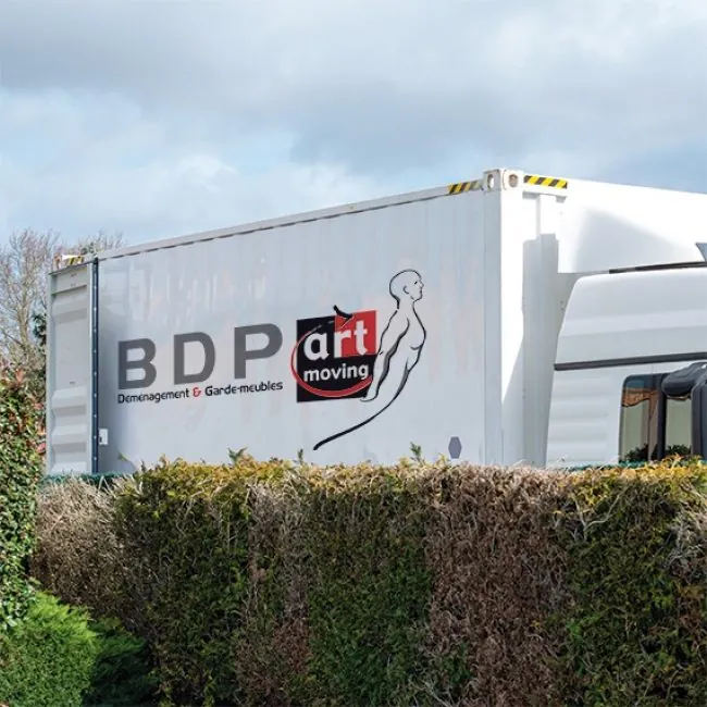 Camion de déménagement BDP-ARTMOVING stationné derrière une haie